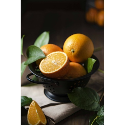 A few juicy oranges in a black bowl with green leaves on a dark wooden background